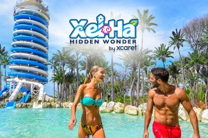 Excursão Xel-Há Tudo Incluído - Casal a divertir-se na piscina natural com o escorrega Faro Mirador ao fundo